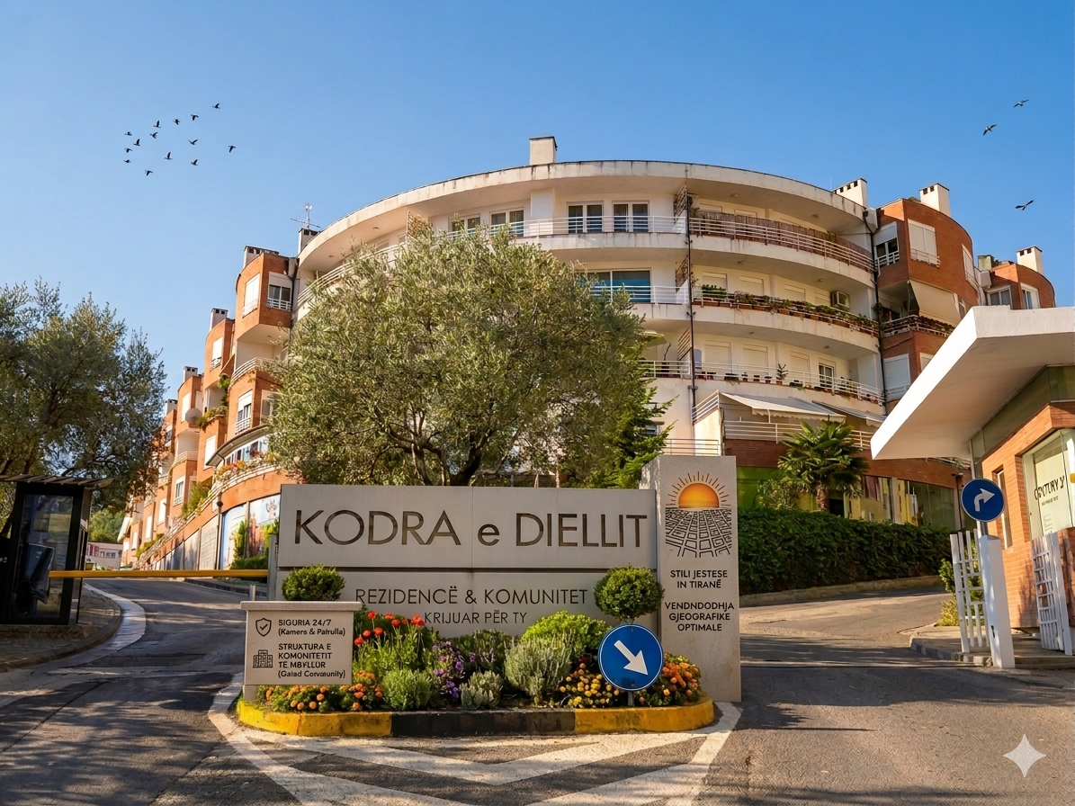 Pamje hyrëse e Rezidencës Kodra e Diellit në Tiranë. Tregohet monumenti kryesor i gurit me mbishkrimet 'Kodra e Diellit' dhe 'Rezidencë & Komunitet Krijuar Për Ty', i rrethuar nga një rrethrrotullim me lule dhe pemë ulliri. Në sfond duket pallati rrethor me tulla të kuqe nën një qiell të kthjellët me zogj.